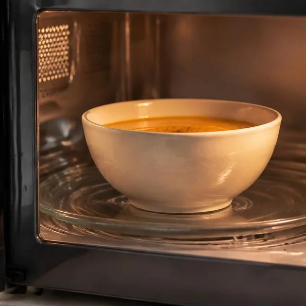 Schale mit Suppe in einer geöffneten Mikrowelle